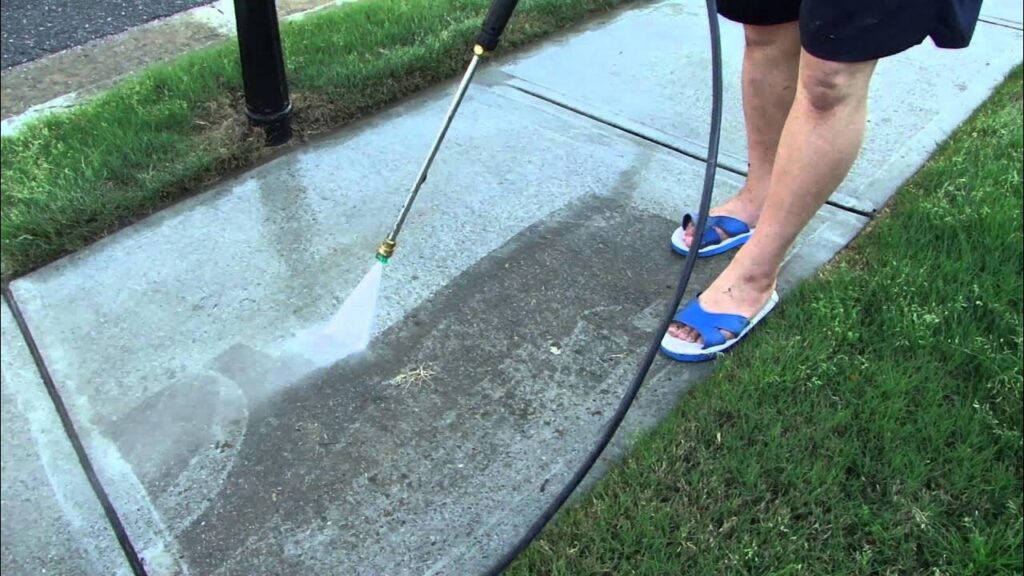 Person using a pressure washer to clean a concrete sidewalk